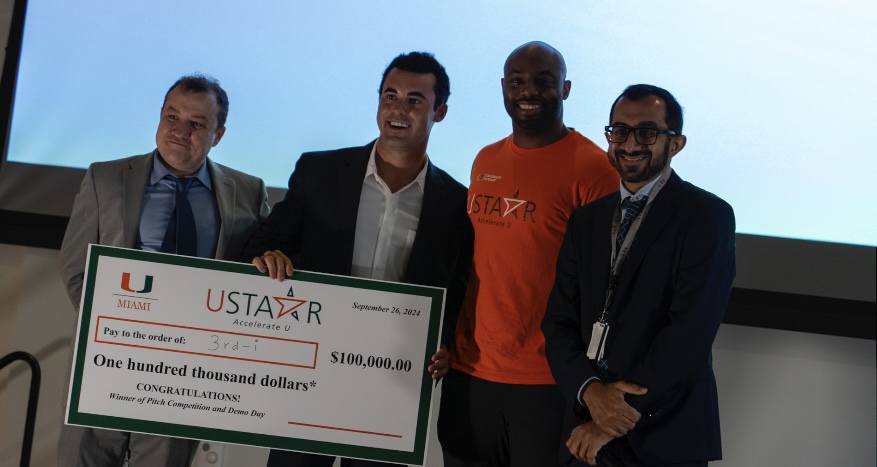 Dillon Abend on stage at the University of Miami holding the USTAAR Accelerate U check made out to 3rd-i for one hundred thousand dollars
